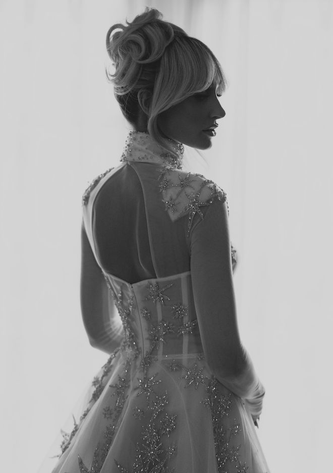 The bride looking over her shoulder with her hair in a bun wearing a long sleeve sheer wedding dress with crystal embellishments that look like snowflakes. 