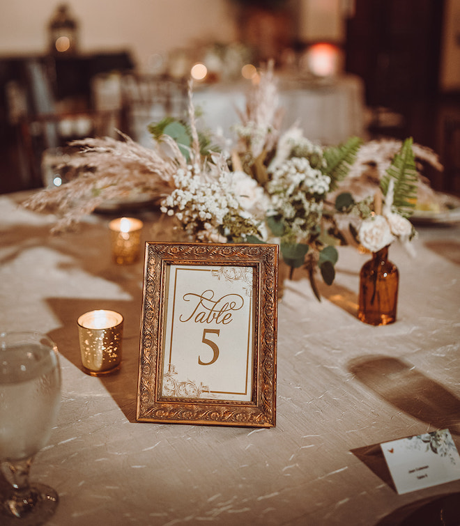 A gold frame with "Table 5" in the center of a reception table with bohemian style florals and candles. 