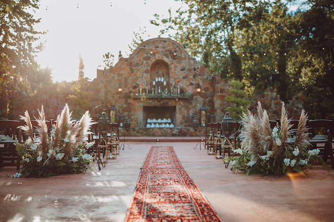 The alfresco ceremony space at Madera Estates with Pampas grass floral arrangements and a red carpet leading to the altar.