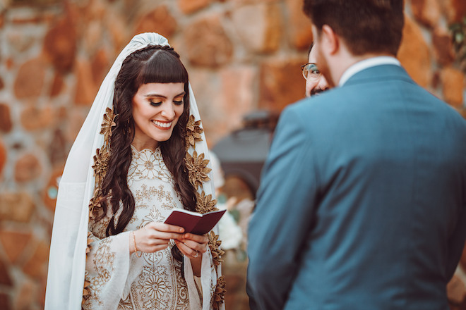 The bride smiling looking down at a red book during the alfresco ceremony. 