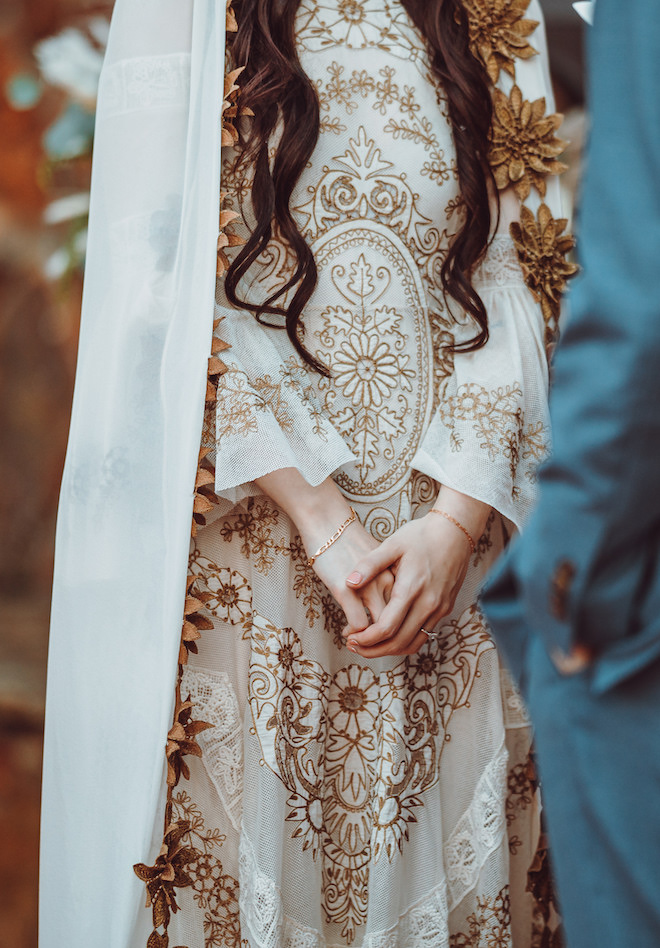 An intricate ivory and gold bohemian gown and a cathedral veil with brown flowers on the trim.