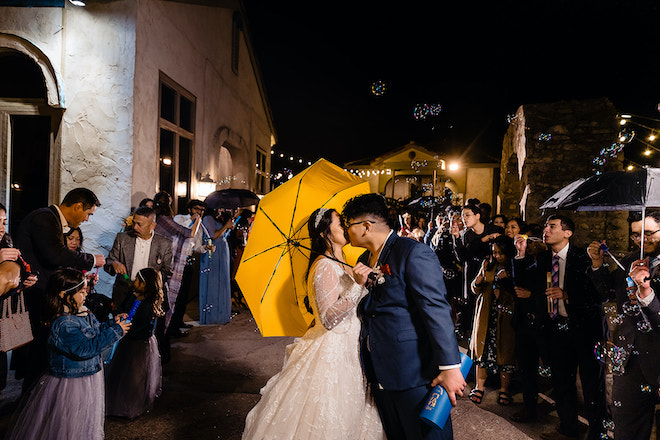 The bride and groom kissing during their bubble sendoff. The bride is holding a yellow umbrella. 