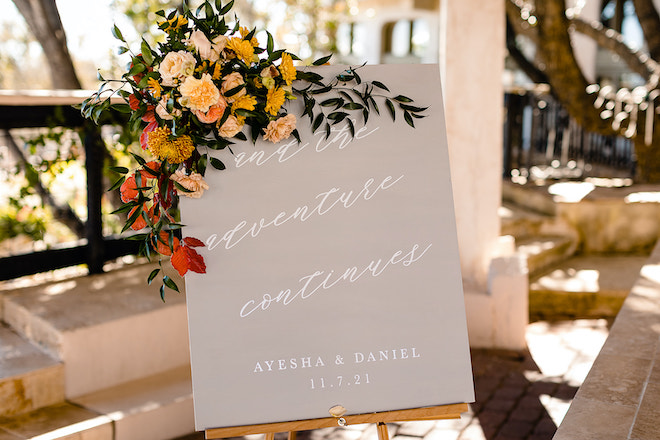 A gray sign that says in white cursive "and the adventure continues, Ayesha & Daniel, 11.7.21" 