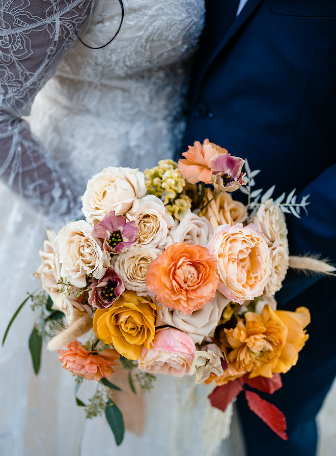 A bouquet with florals in shades of orange, yellow, blush and sand. 
