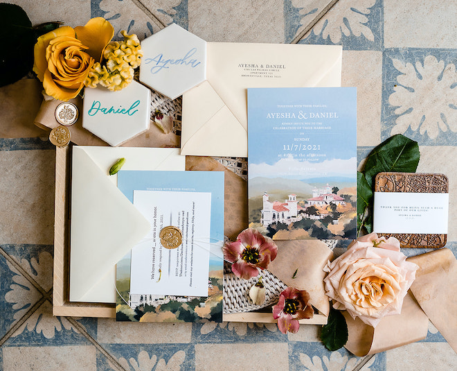 An invitation suite for Ayesha and Daniel including a print of the venue on the invitation, tiles with their names on them and yellow and blush florals. 
