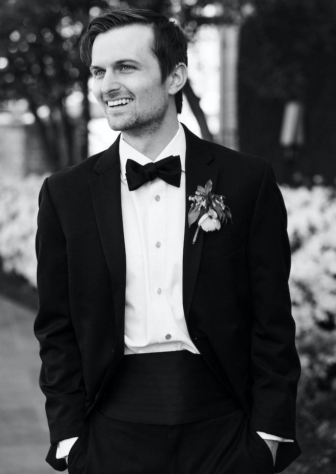 The groom smiling wearing his tuxedo with his hands in his pockets. 