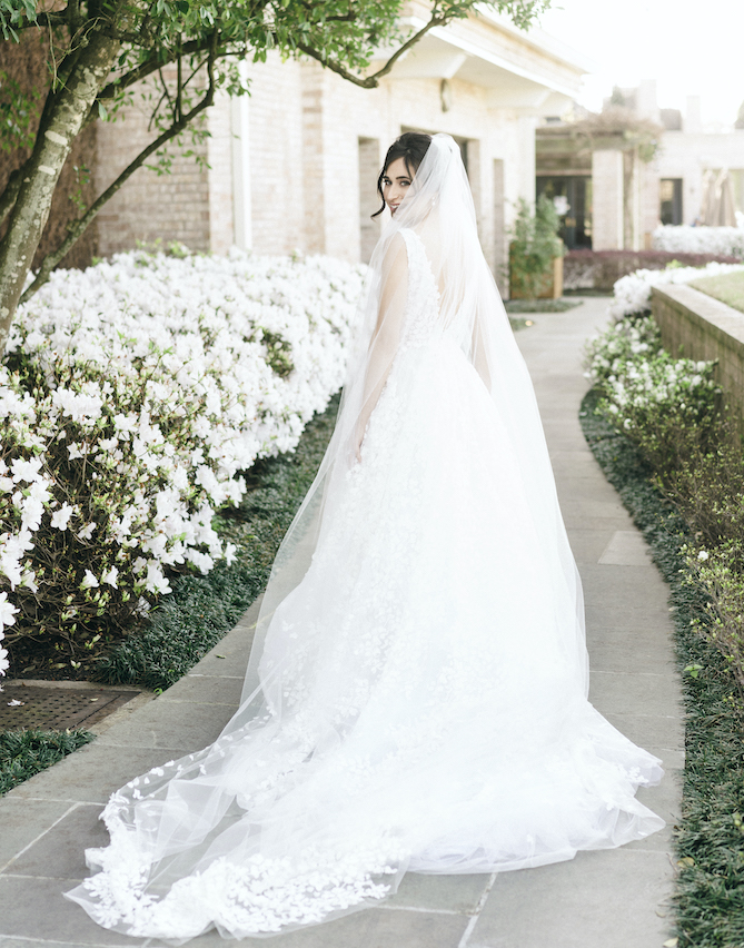 A bride walking down a sidewalk looking back with her custom veil and Romona Keveza gown for her wedding in Houston. 