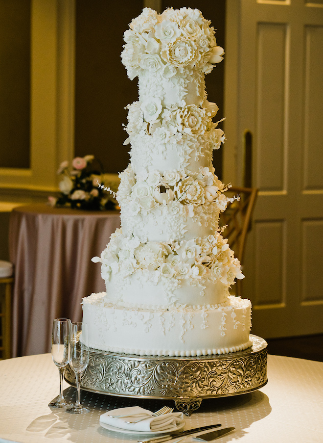 A five tier white wedding cake with floral garnishes. 