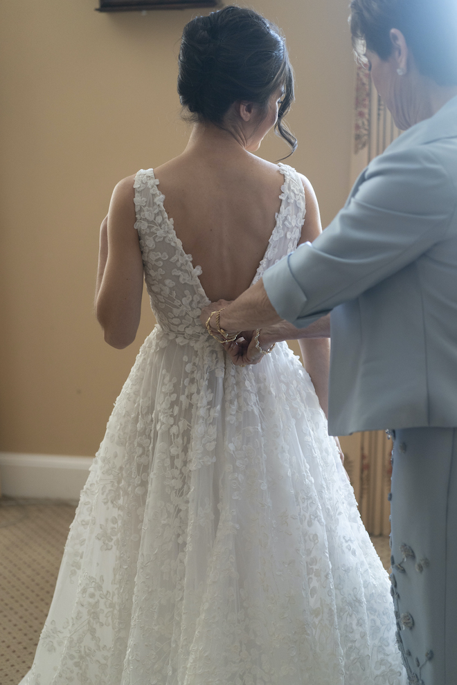 A woman buttoning the back of the bride's Romona Keveza gown.