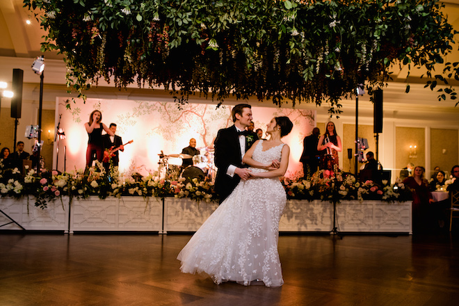 The bride and groom dancing under the wisteria-inspired florals with the band playing in the background. 