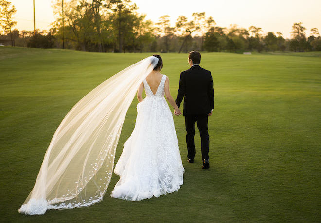 The bride and groom holding hands walking on a golf course with the bride's custom veil blowing in the wind. 