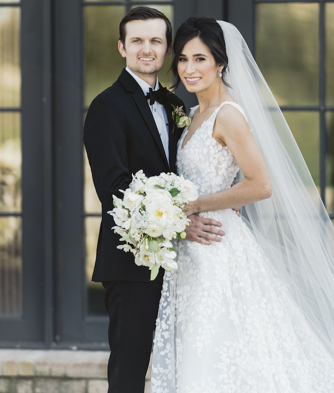 Bride and groom smiling with the bride holding a green and white bouquet in her hands. 