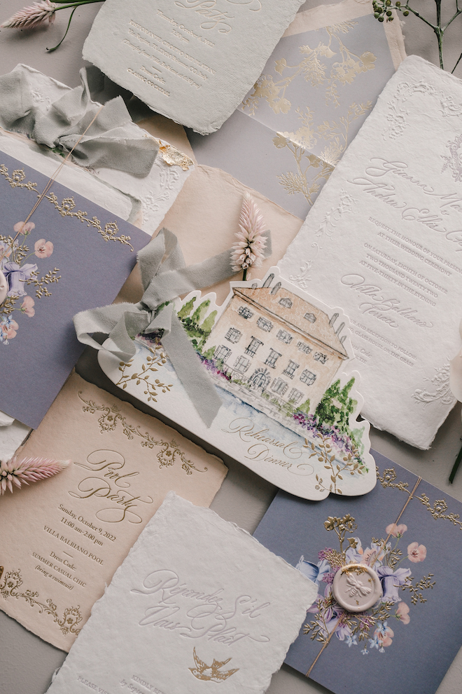 Handmade paper and textured white and purple invitation suites with a house and florals drawing. 