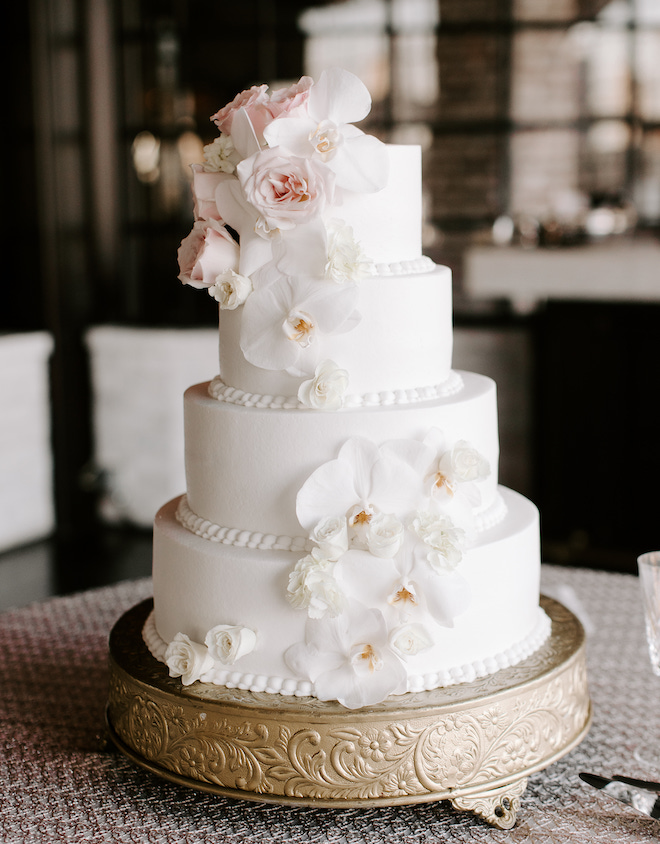 A four-tier wedding cake with white and blush florals garnishing the tiers. 
