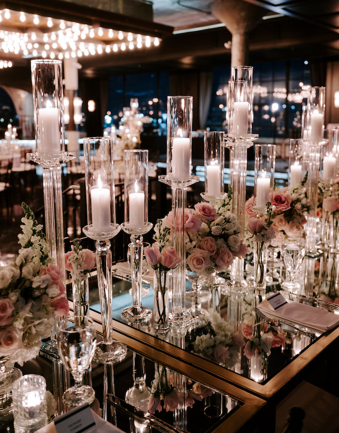Pillar candles and white and blush florals on the mirrored family-style table. 