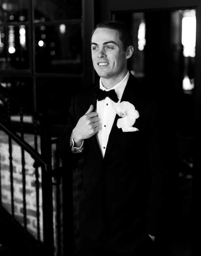 The groom smiling in his tuxedo with an orchid pinned to his suit jacket.