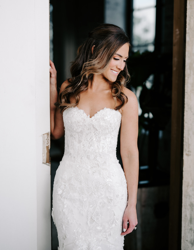 The bride smiling and wearing a lace strapless wedding gown.