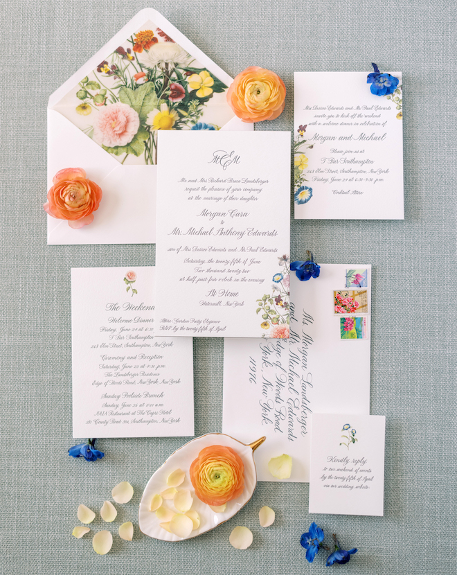 A white invitation suite with black calligraphy with colorful flowers on the edges of the invitations. 