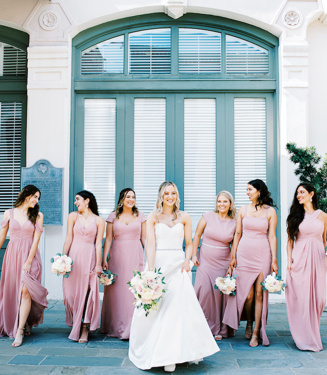 A bride and her bridesmaids in pink dresses walking in front of The Tremont House.