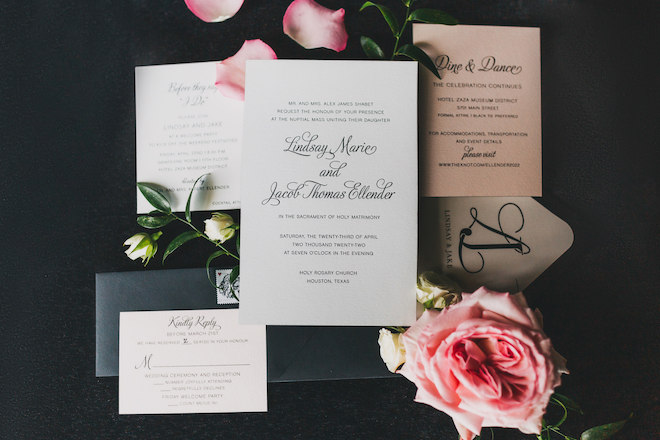 A black and white invitation suite with pink florals around it. 
