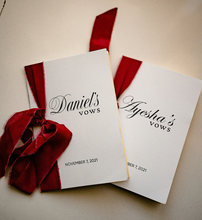 Two paper books with a red bow tied on the sides of them reading "Daniel's Vows" and "Ayesha's Vows November 7, 2021."