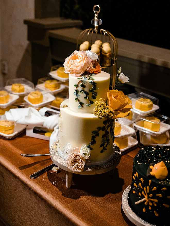 A two-tier white cake with peach and gold florals and greenery painted in icing. 