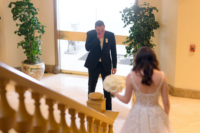 The groom is in awe as he sees his bride walk down the stairs for the couple's first look before the ceremony. 