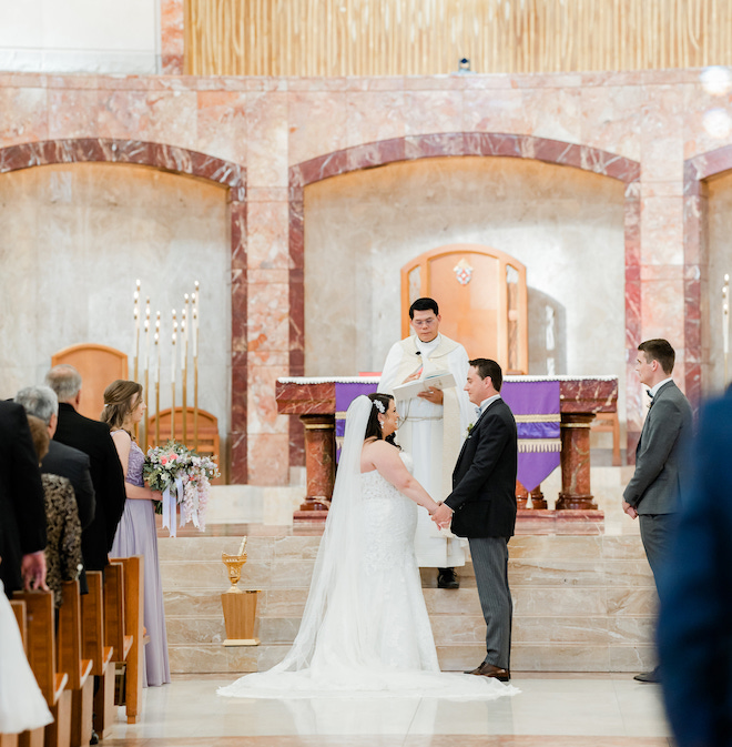 A bride and groom holding hands during their wedding ceremony in a church. 