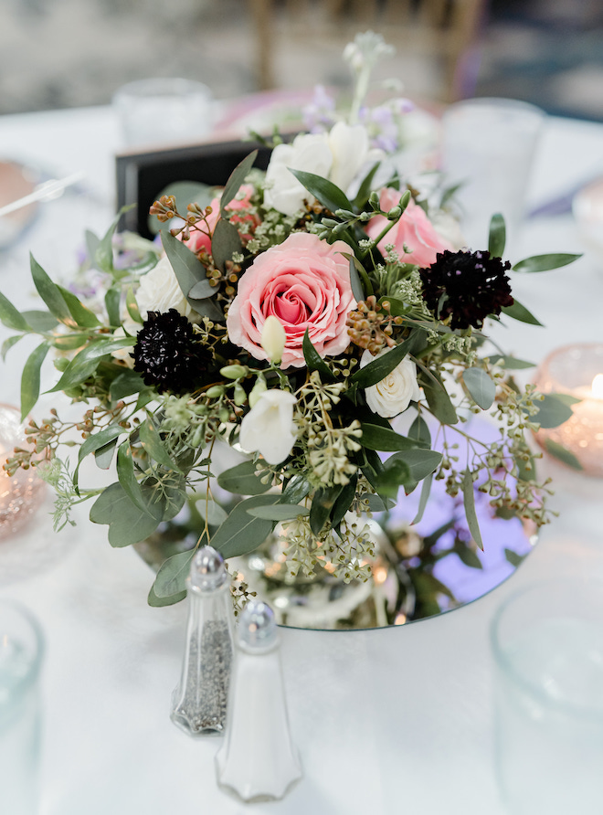 A floral arrangement on a reception table with greenery, white and pink florals. 