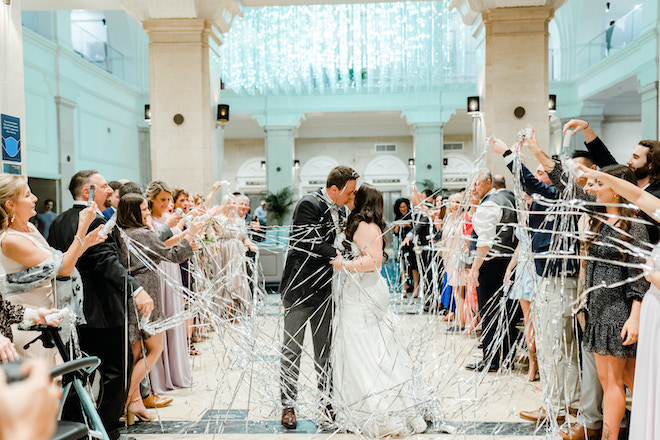 The bride and groom kissing during their sendoff with guests throwing streamers.