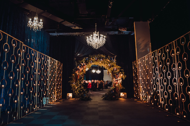 An indoor wedding at The Ballroom at Bayou Place with event lighting by Bright Star Productions, a floral arch and panels holding lit votives.