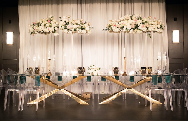 A long gold reception table with tall floral arrangements with white, green and blush florals. 