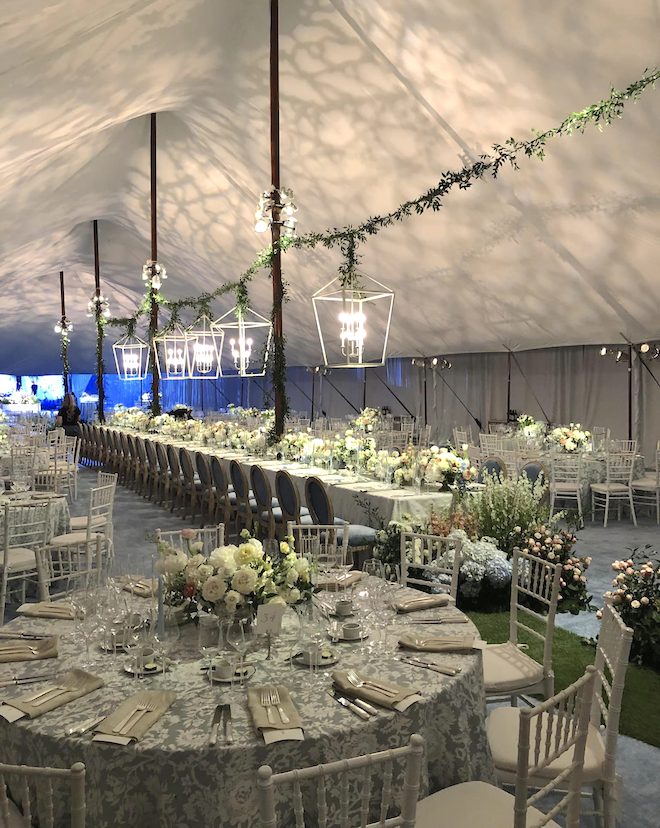 A tented wedding with hanging lanterns, greenery and banquet tables in Houston, TX.