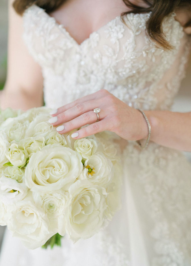 The bride places her left hand on the white, rose-filled wedding bouquet to display her wedding ring. 