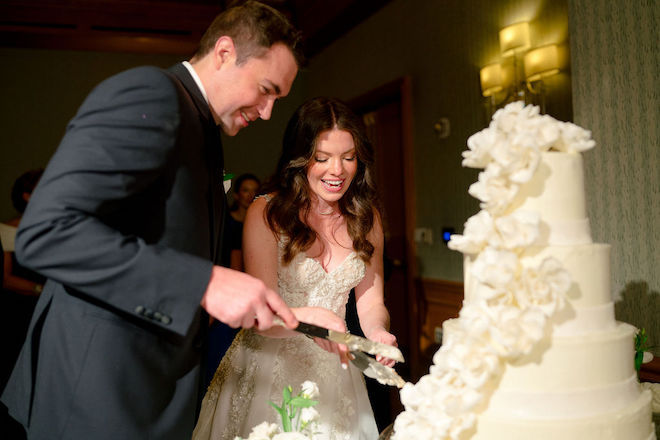 The bride and groom cut a multi-tiered white wedding cake at their ballroom wedding in Houston. 
