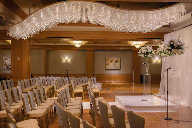 A wedding ceremony decorated with ceremony chairs, simple tall floral arrangements and sheer draping in Houston. 