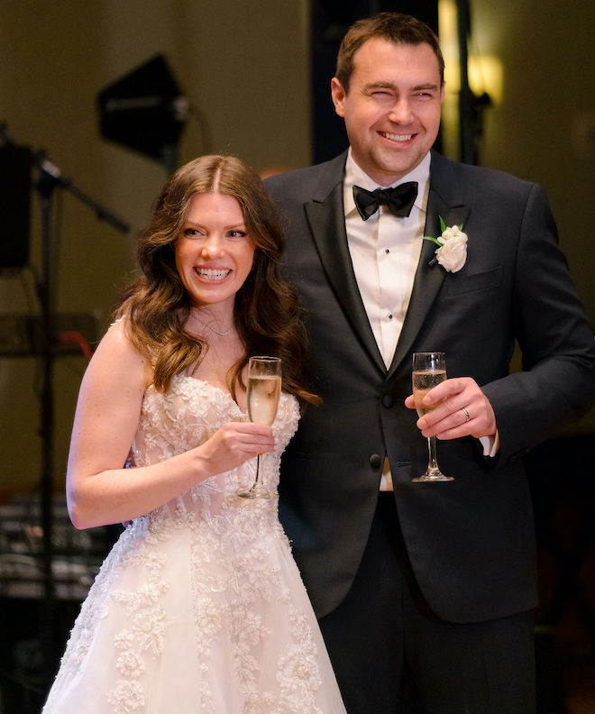 The bride and groom smile as they share a toast with their wedding guests in the hotel ballroom. 