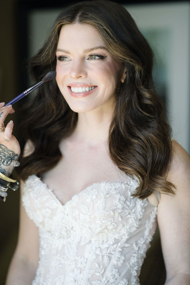 The bride smiles as she gets her makeup retouched before her wedding ceremony. 