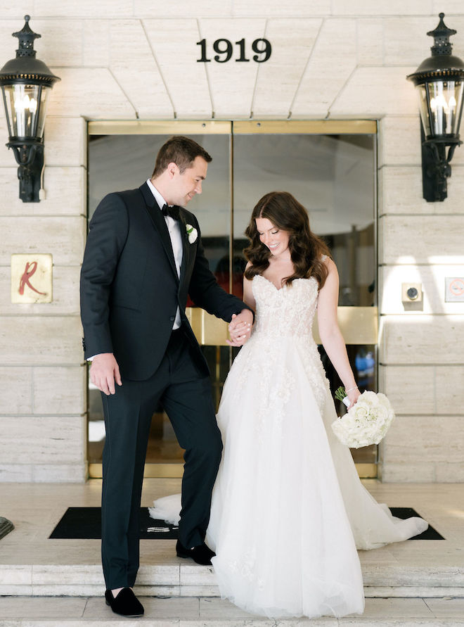 The bride and groom hold hands as they walk down the steps outside their Houston hotel wedding venue.