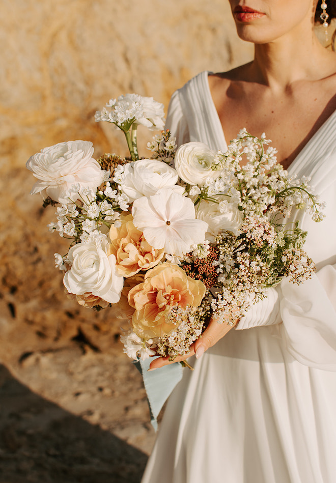 The bride holding a bouquet of white and muted orange florals. 
