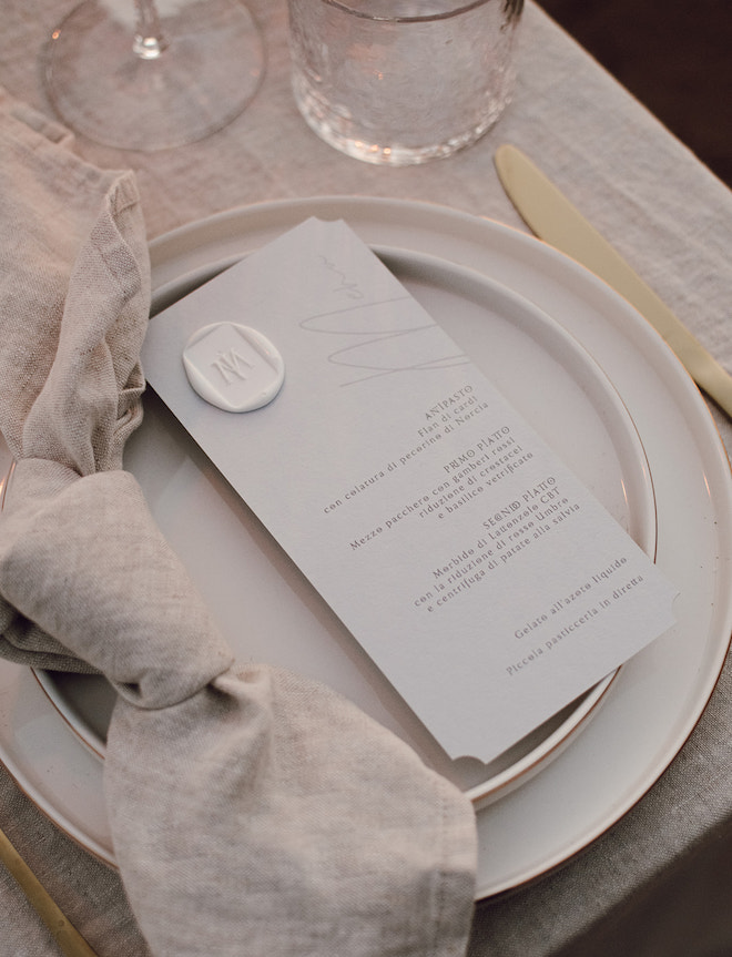 A menu with a wax seal on a white plate with beige napkins.