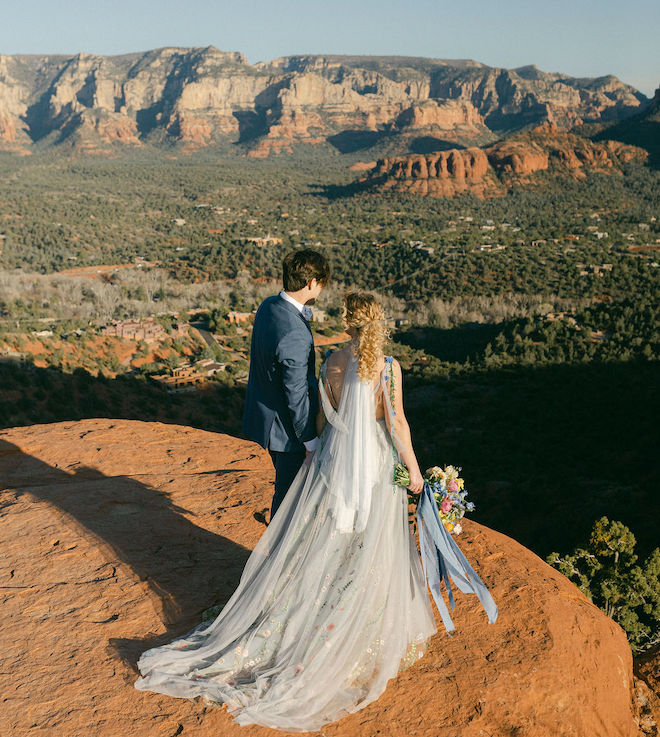 The bride and groom standing on a mountain overlooking the natural views of Sedona, Arizona. 