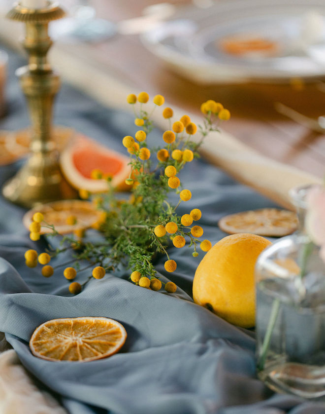 Fresh citrus slices and yellow florals on a blue tablecloth at the reception table. 