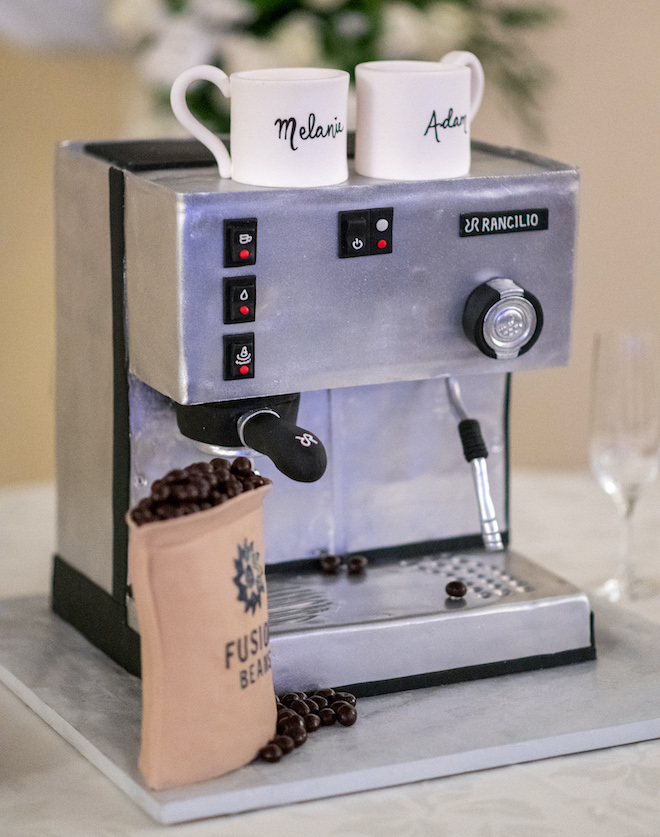 An espresso machine groom's cake with coffee beans and coffee mugs with Melanie and Adam's names on them. 