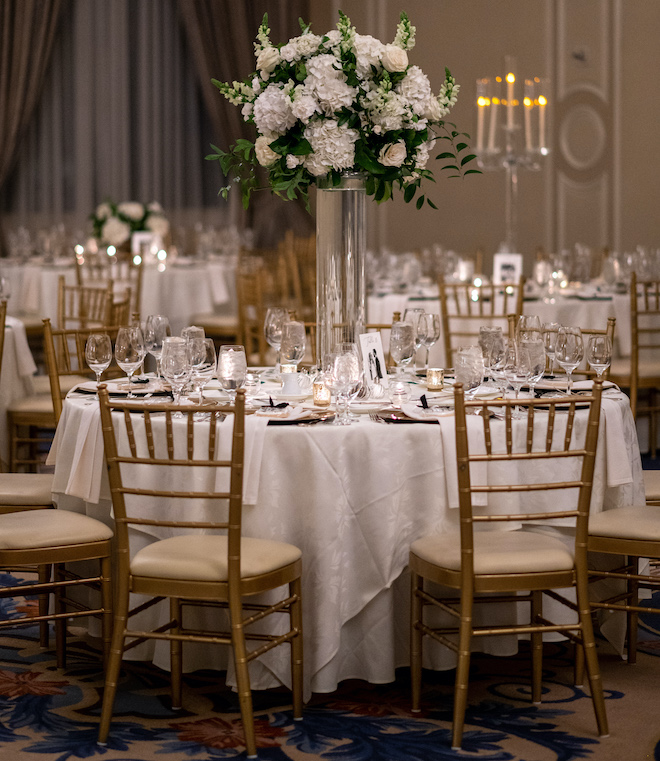 A round reception table with a centerpiece of greenery and white florals. 
