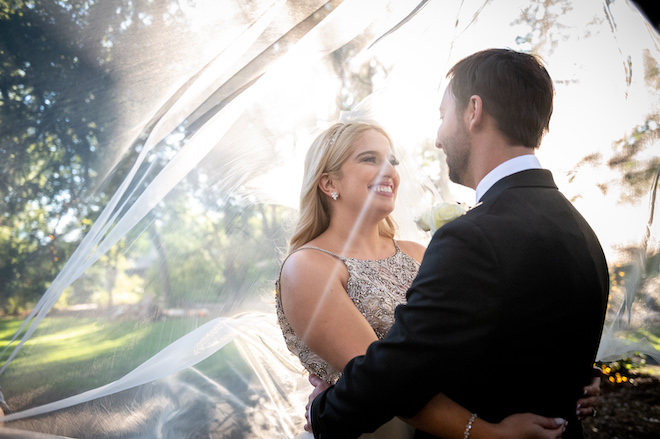 The bride smiling at the groom with her veil over them. 