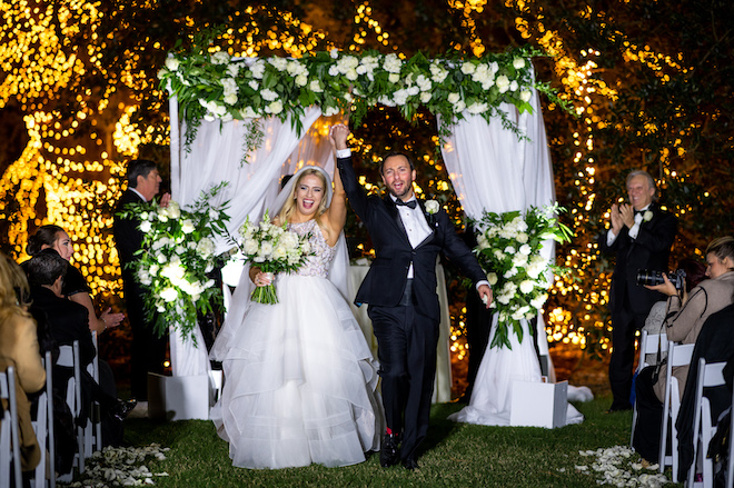 The bride and groom cheering as they walk back down the aisle of their outdoor twilight wedding ceremony.