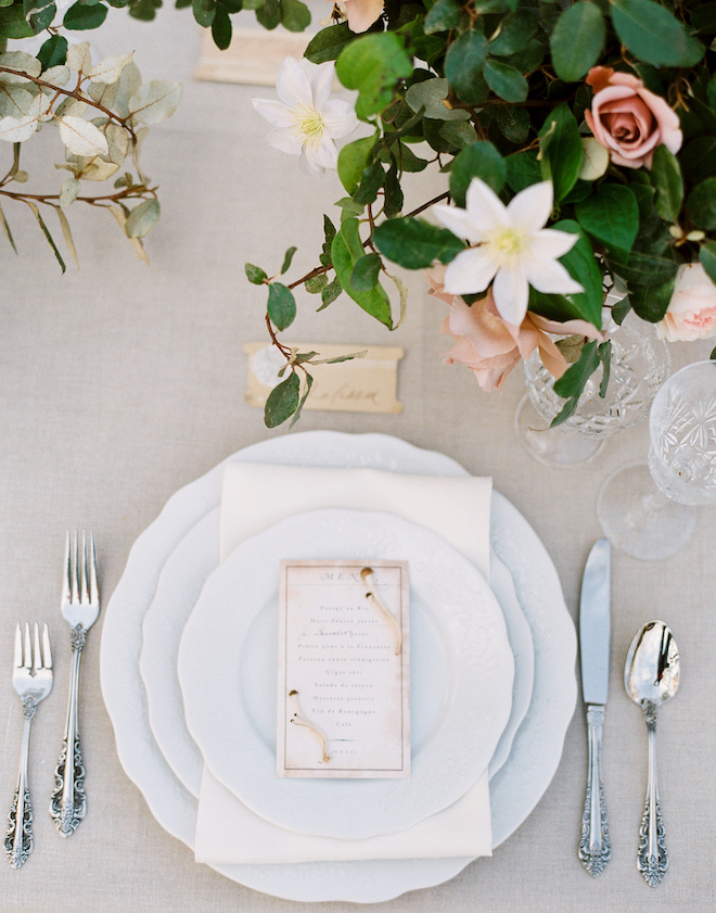 White plates with silverware with a cream menu and greenery, white and blush florals for an intimate wedding editorial.