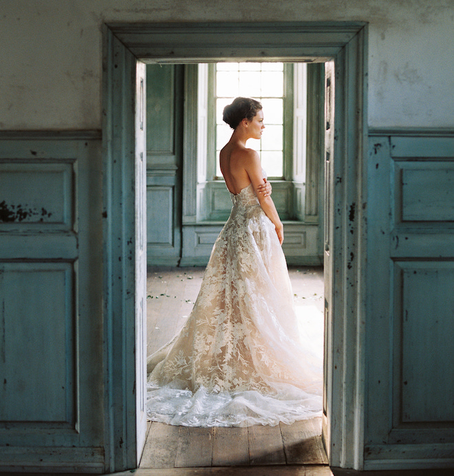 A bride wearing a strapless lace gown standing in a blue door frame. 