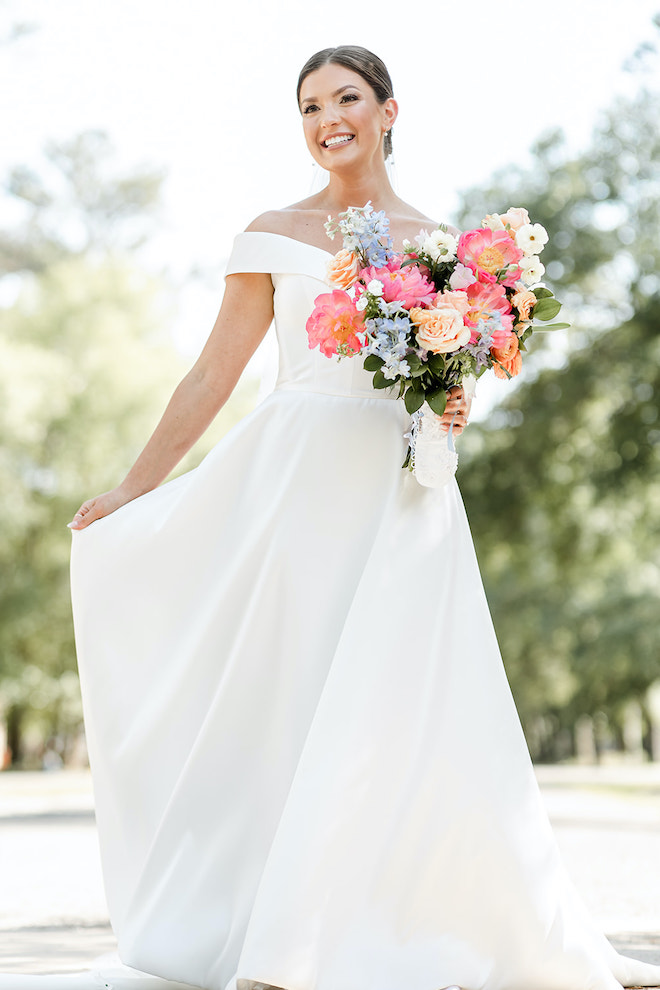 The bride smiles at her portraits and holds her wedding bouquet filled with pastel spring florals. 